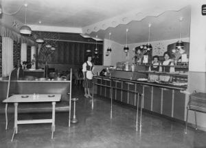 Tre bunadskledde ansatte på Fønix kafe i et tidstypisk kafeinteriør, fotografert i 1960. Hva damene heter er ikke registrert på Mjøsmuseets arkivkort. (Foto: Mjøsmuseet).